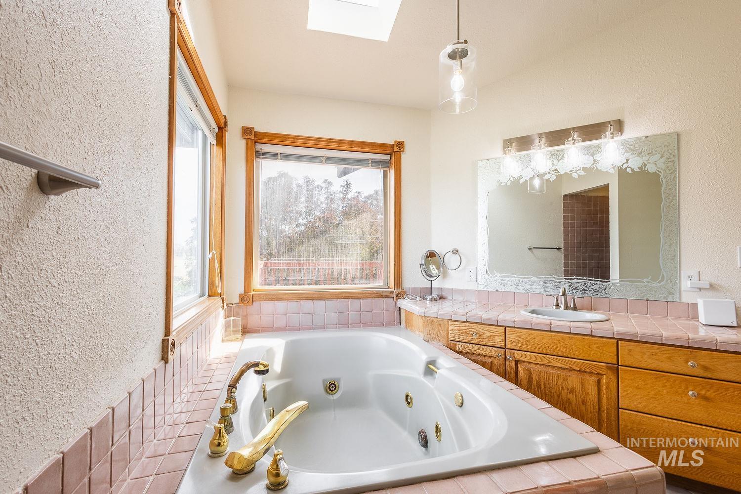 Full bathroom with a textured wall, a skylight, vanity, and a tub with jets