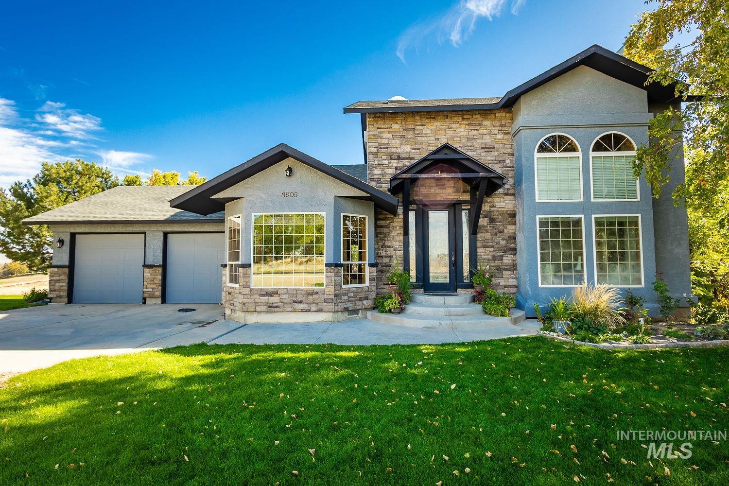 View of front of property with a front lawn, concrete driveway, a garage, and stone siding