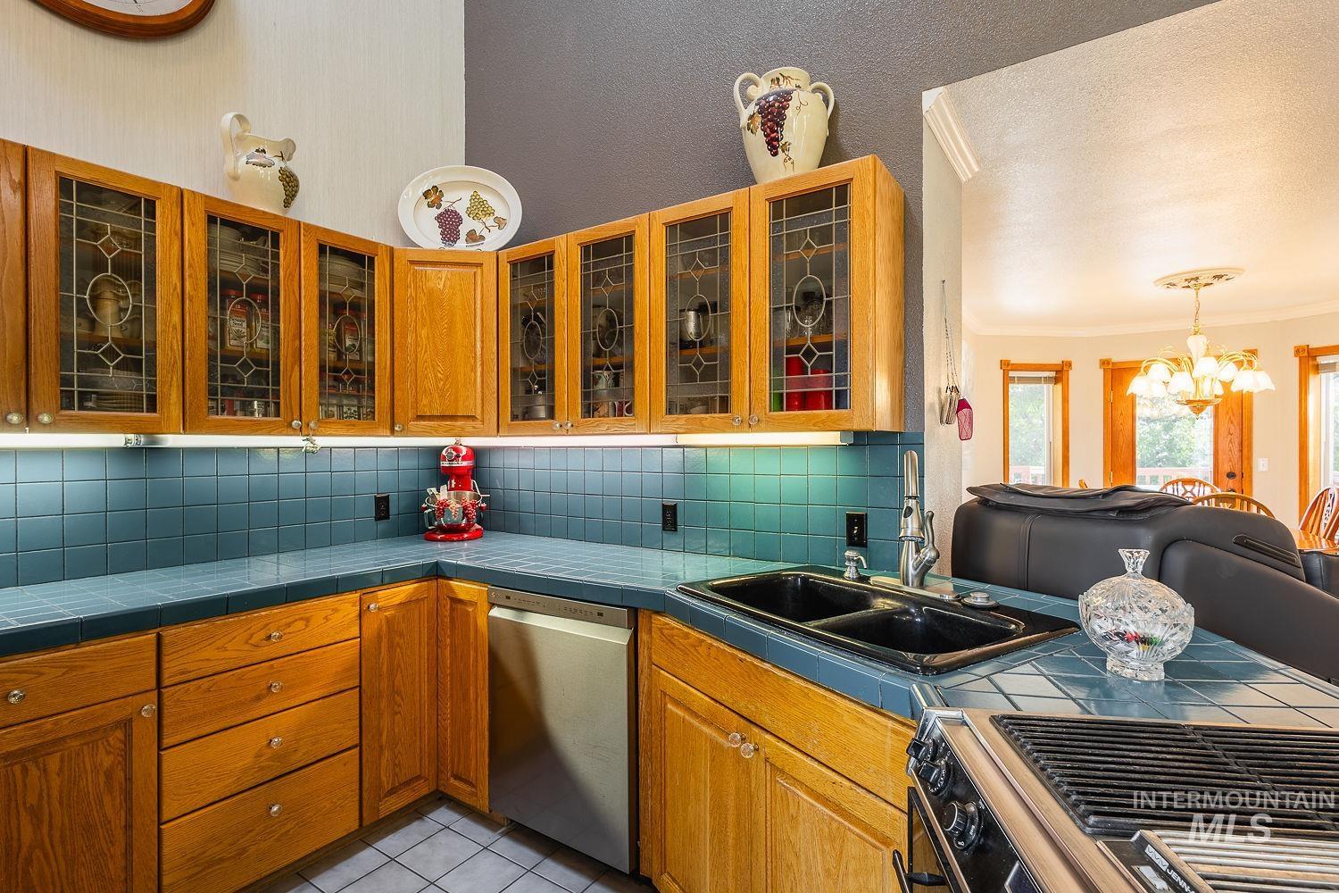 Kitchen with decorative backsplash, stainless steel appliances, crown molding, a chandelier, and light tile patterned flooring
