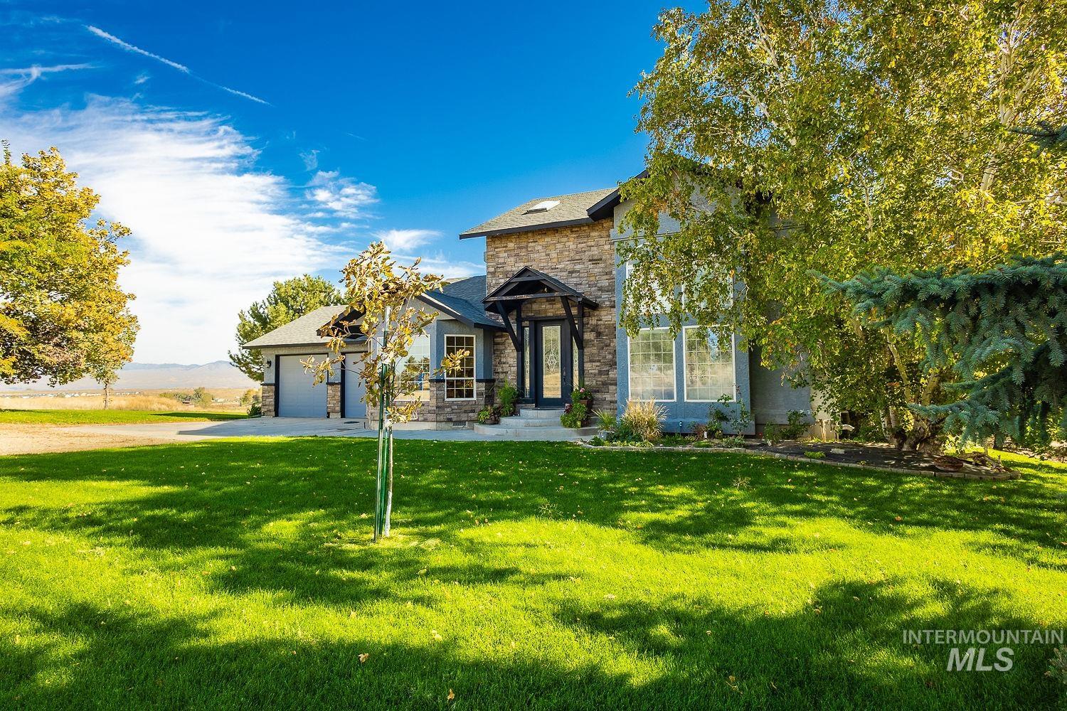 View of front of home featuring stone siding, a front lawn, driveway, a garage, and a shingled roof