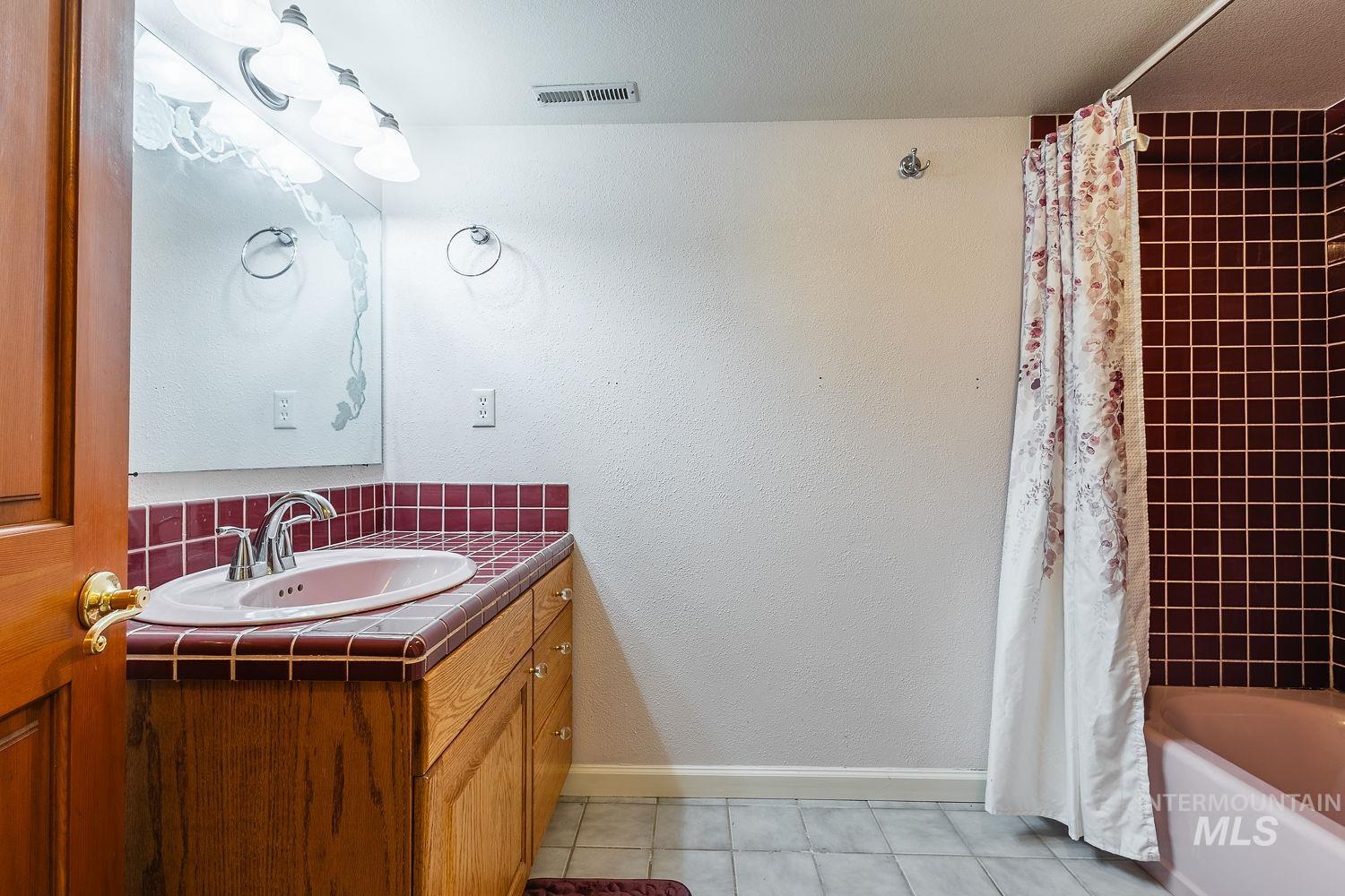Full bath with vanity, light tile patterned flooring, shower / tub combo, a textured wall, and backsplash