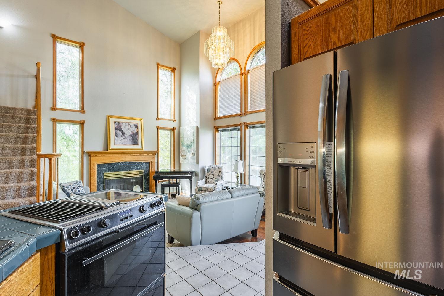 Kitchen featuring stainless steel fridge with ice dispenser, electric range, light tile patterned floors, brown cabinetry, and pendant lighting