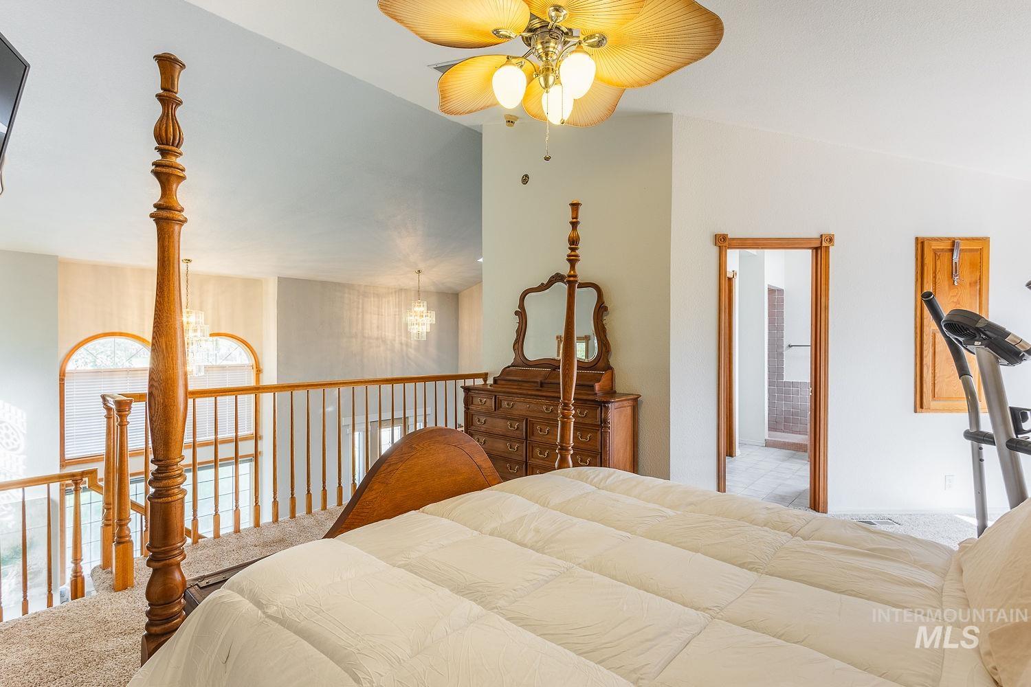 Bedroom featuring carpet, a ceiling fan, vaulted ceiling, ensuite bathroom, and a chandelier