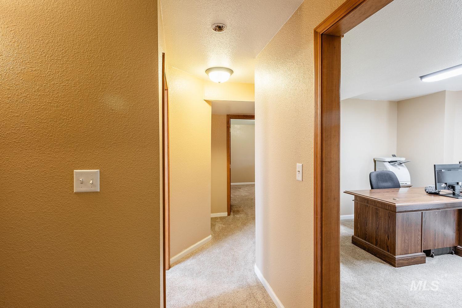 Hallway with a desk, a textured wall, a textured ceiling, and light colored carpet