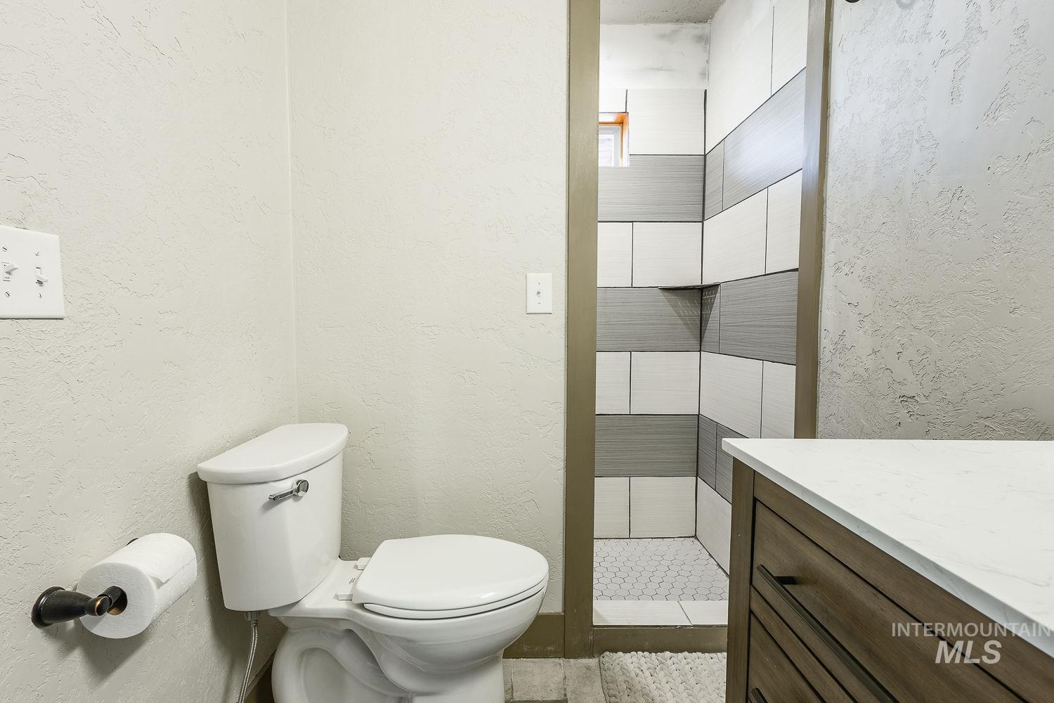 Bathroom featuring a textured wall, a tile shower, and vanity
