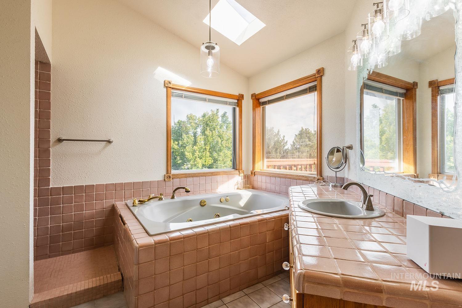 Bathroom featuring a skylight, vaulted ceiling, a tub with jets, vanity, and a textured wall