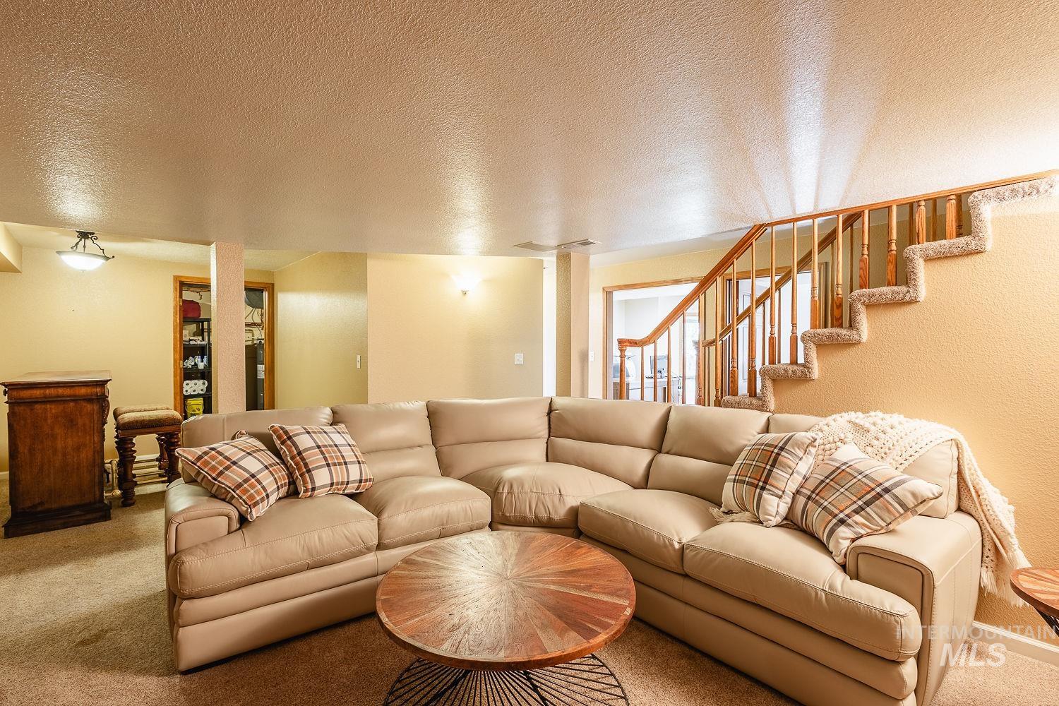 Carpeted living room featuring a textured ceiling and stairs