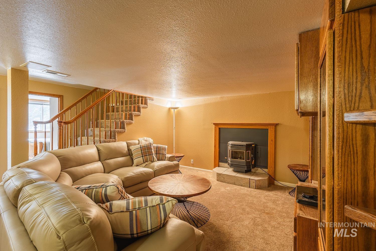Carpeted living area featuring stairs, a textured ceiling, and a wood stove