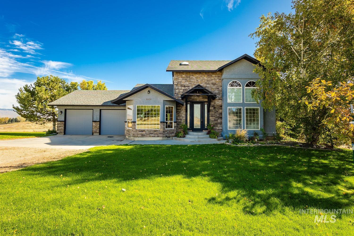 View of front of property featuring driveway, a front yard, a garage, a shingled roof, and stone siding