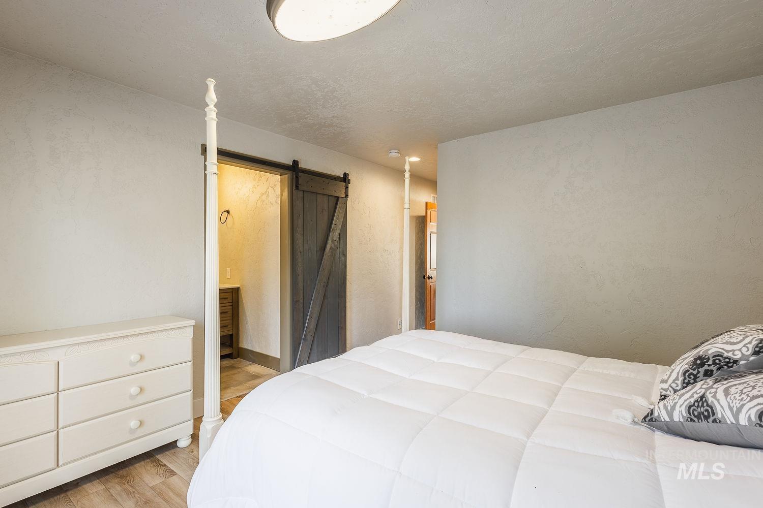 Bedroom with a barn door, light wood finished floors, and a textured ceiling
