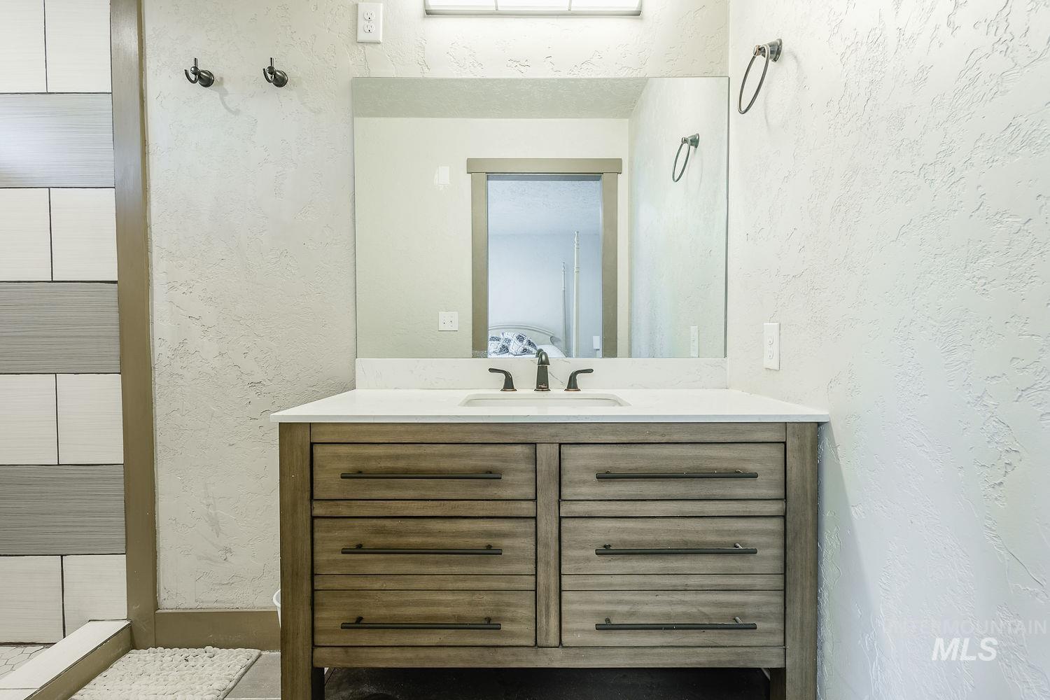 Bathroom with a textured wall, vanity, and tiled shower