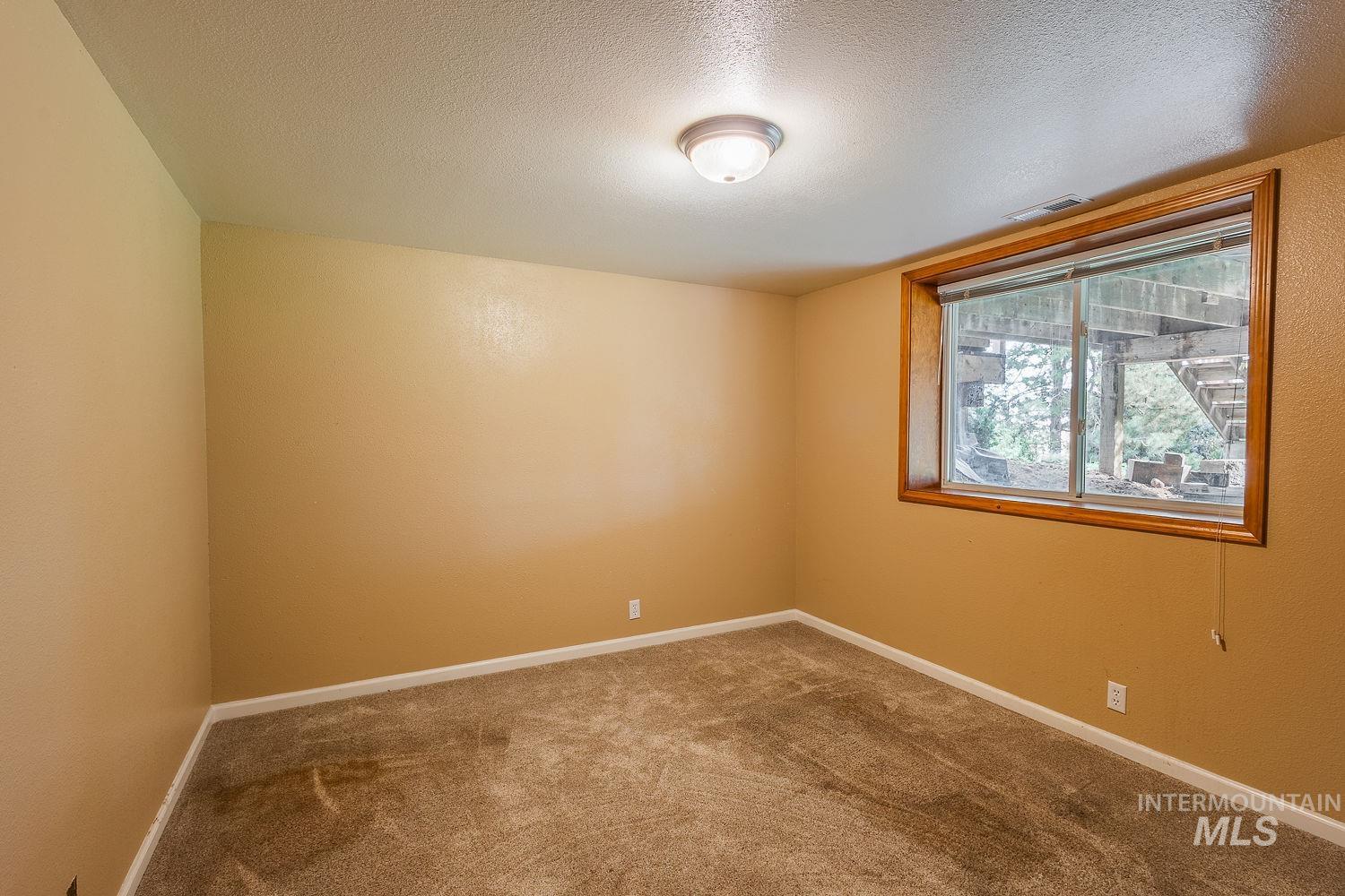 Carpeted spare room with a textured ceiling and baseboards