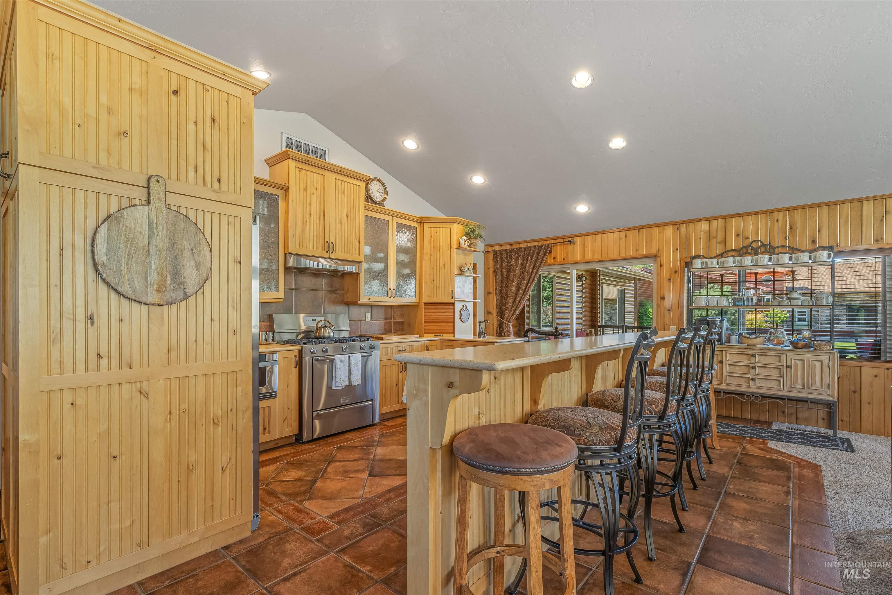 Kitchen with lofted ceiling, a kitchen bar, stainless steel gas range oven, glass insert cabinets, and light countertops