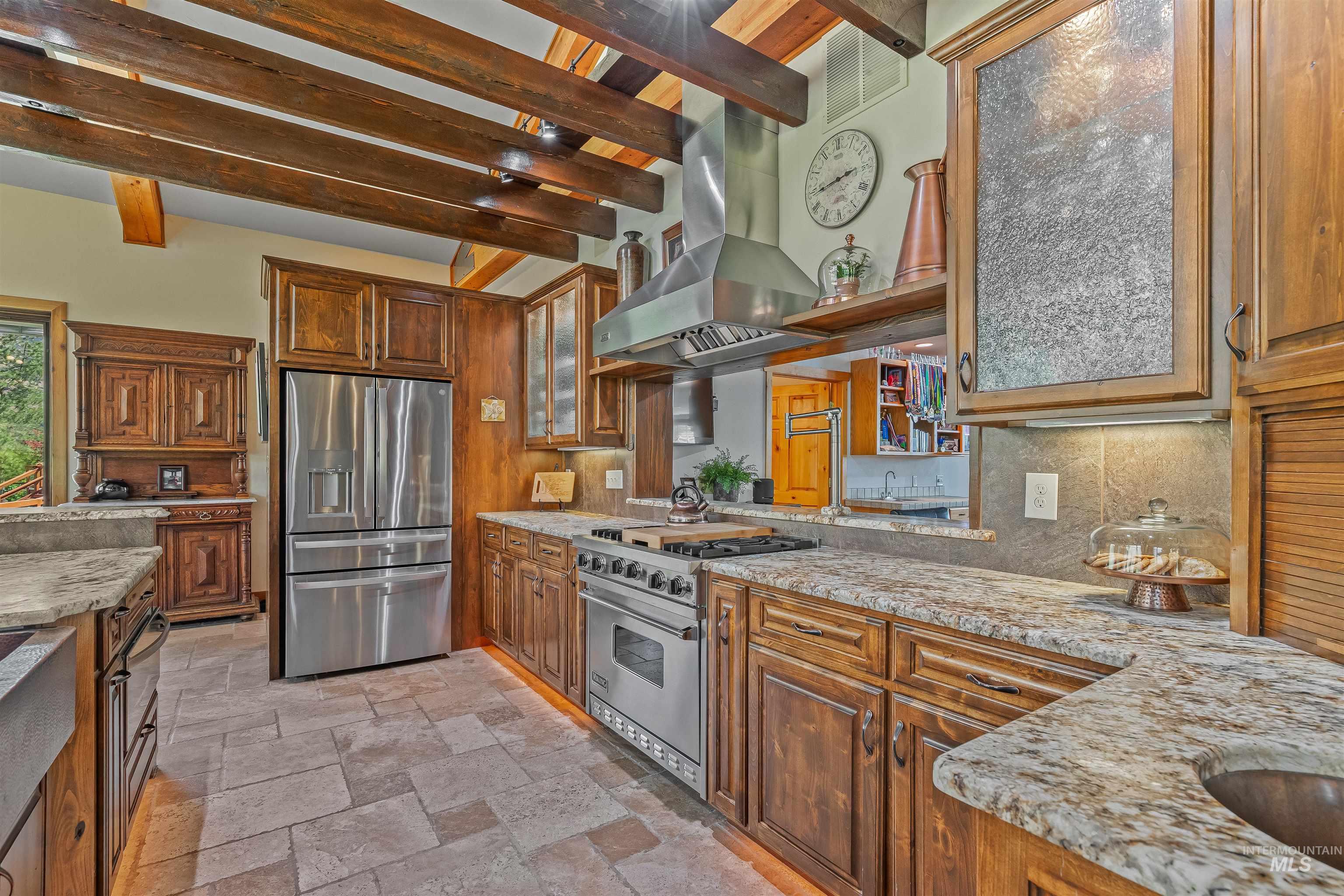 Kitchen featuring backsplash, extractor fan, stainless steel appliances, beam ceiling, and light stone countertops