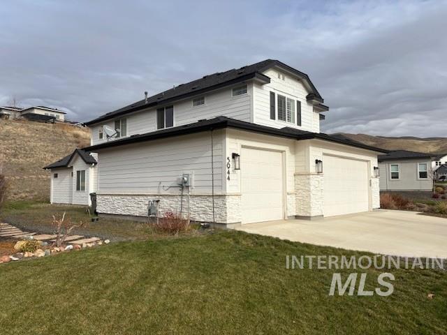 View of property exterior featuring a yard, concrete driveway, a garage, and stone siding