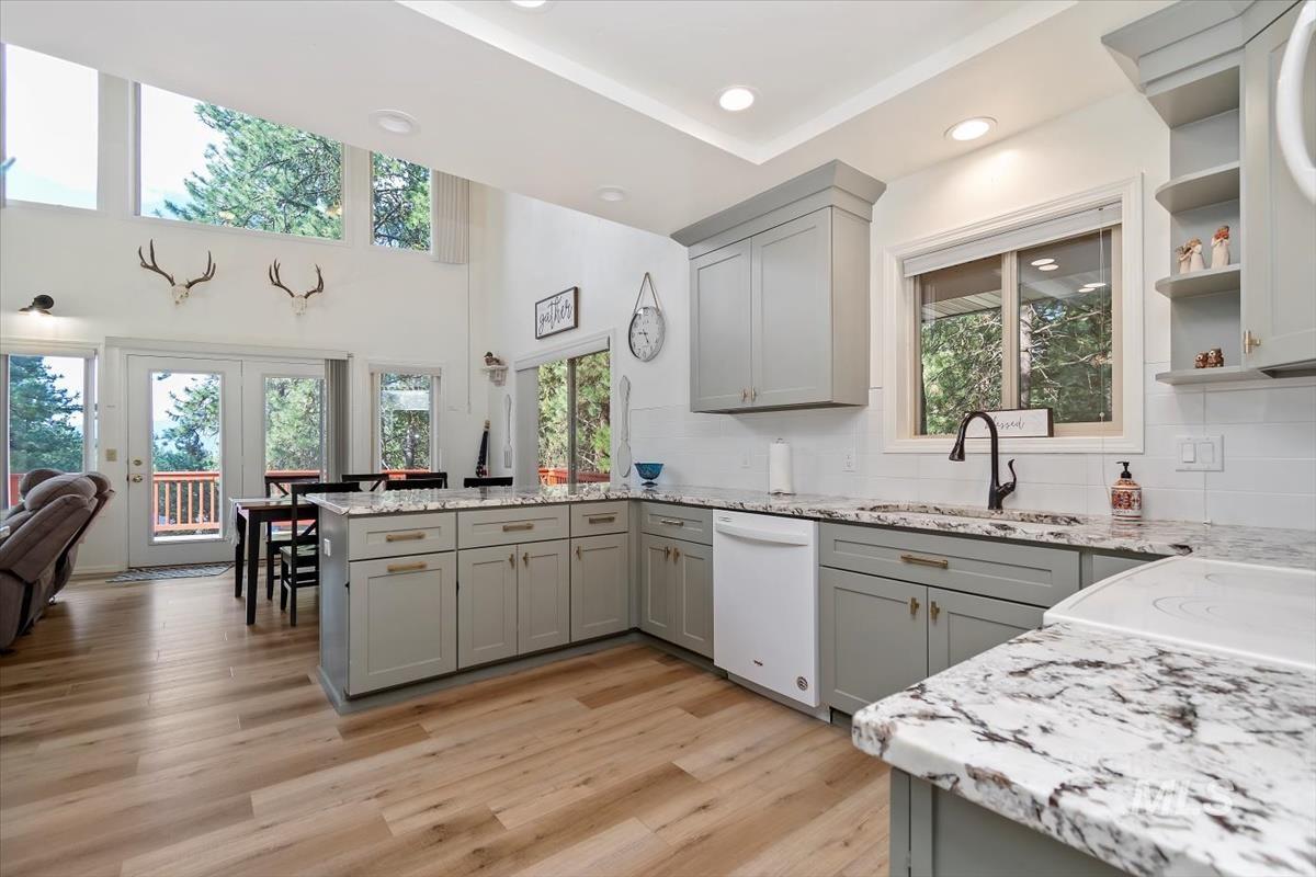 Kitchen featuring gray cabinetry, light stone countertops, light wood finished floors, recessed lighting, and a high ceiling