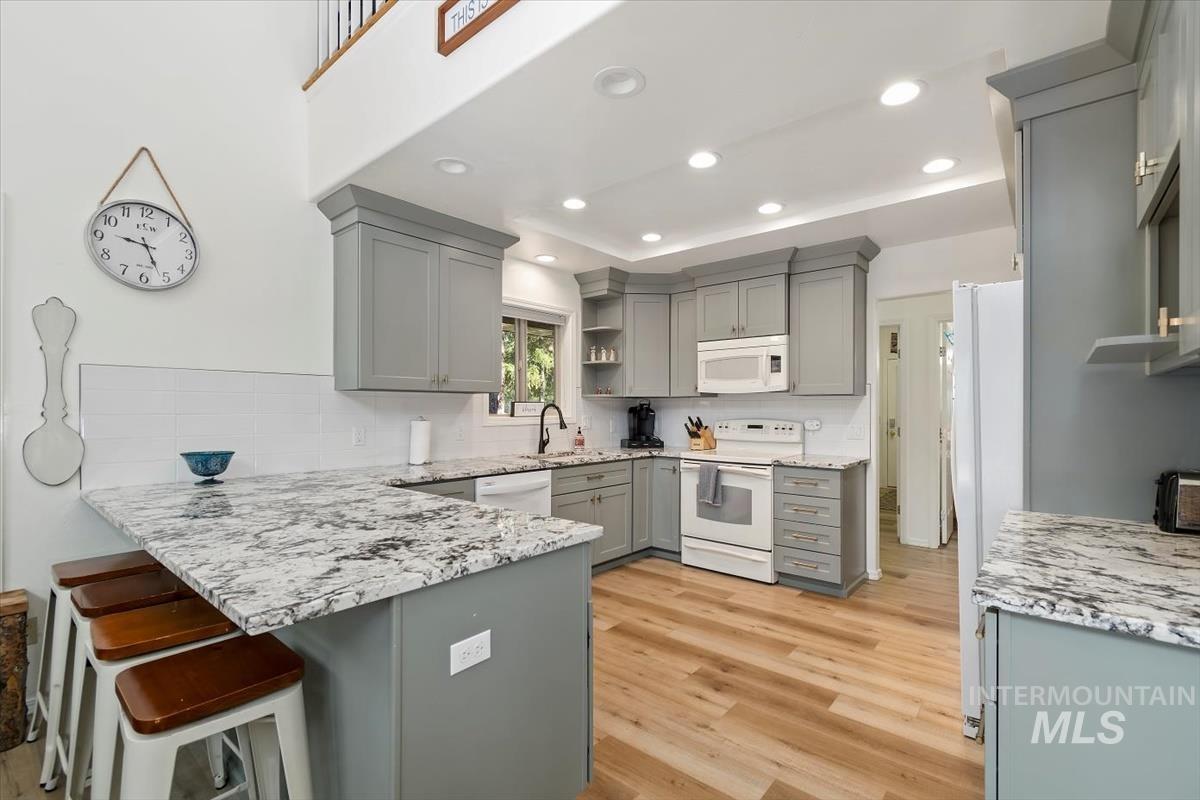 Kitchen featuring open shelves, white appliances, gray cabinetry, light stone counters, and recessed lighting
