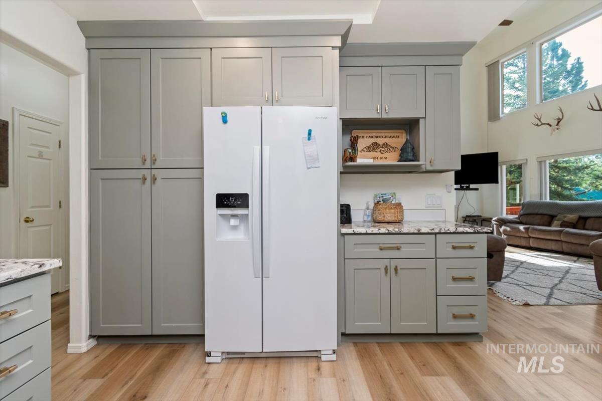 Kitchen with gray cabinets, white refrigerator with ice dispenser, light stone countertops, light wood-type flooring, and a high ceiling