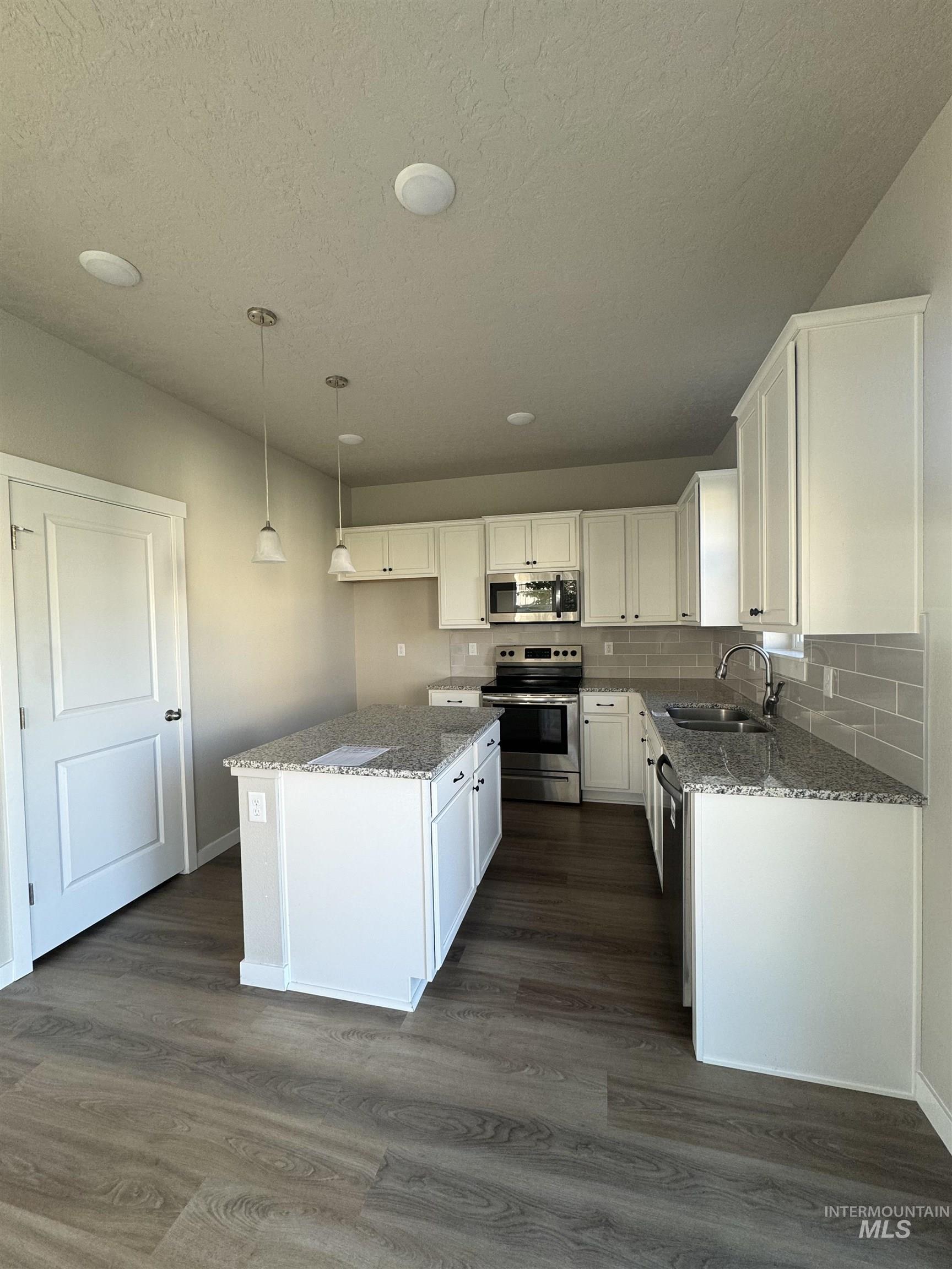 Kitchen featuring dark stone counters, decorative backsplash, stainless steel appliances, dark wood-type flooring, and pendant lighting