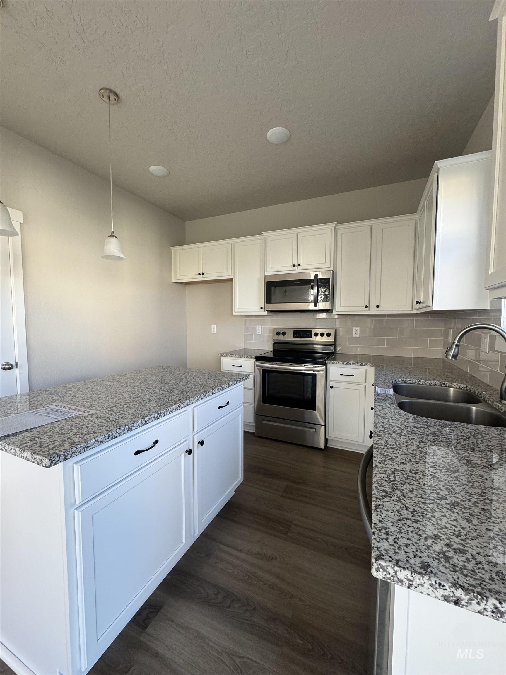Kitchen featuring stainless steel appliances, white cabinets, hanging light fixtures, light stone counters, and decorative backsplash