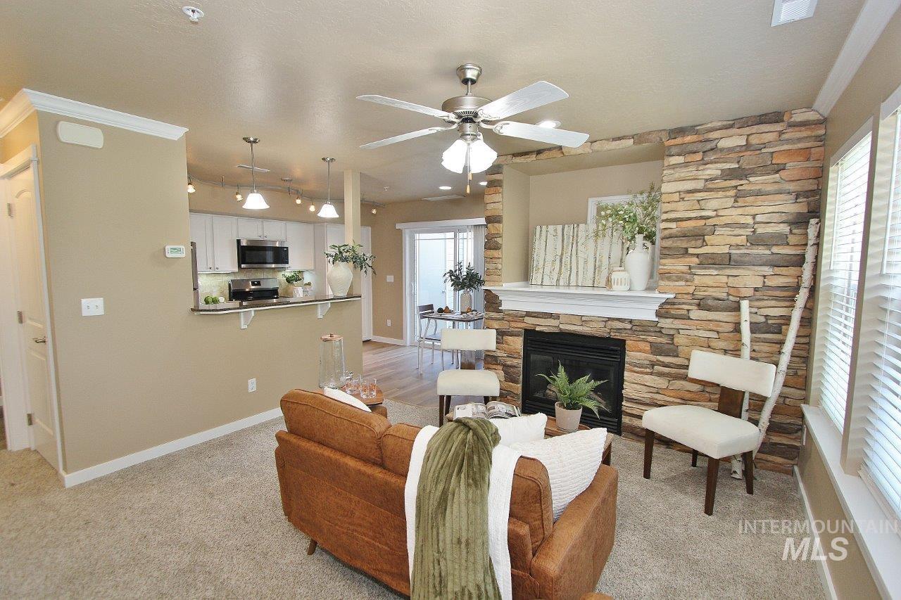 Living area featuring a stone accent wall with a built-in fireplace and white mantel, a ceiling fan with integrated lighting, and carpet flooring