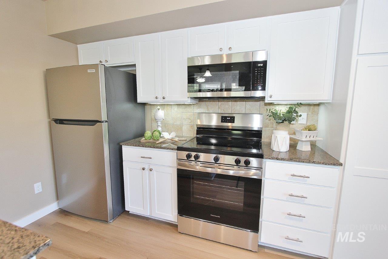 Kitchen with wood-finish flooring, white cabinetry, granite-style countertops, stainless steel appliances, and a tiled backsplash