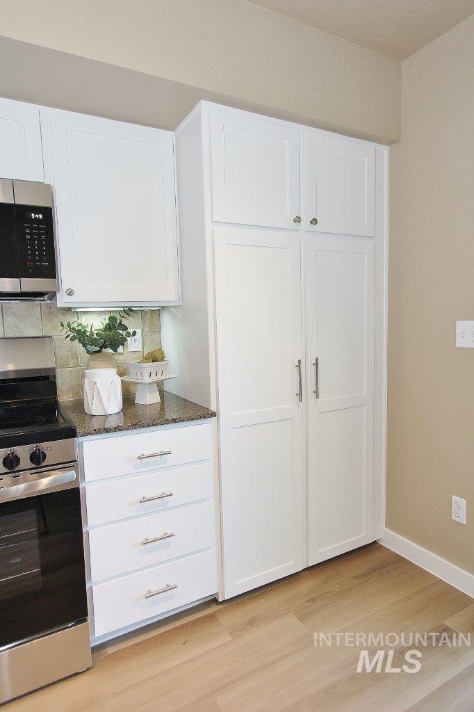 Kitchen featuring white shaker-style cabinetry, a stainless steel range with overhead microwave, a stone-finish countertop, and a light wood-finish flooring