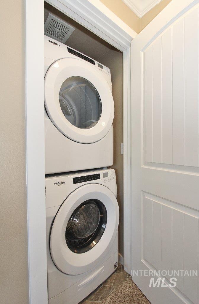 Dedicated laundry closet featuring a stacked white front-loading washer and dryer, tile flooring, and a white paneled door