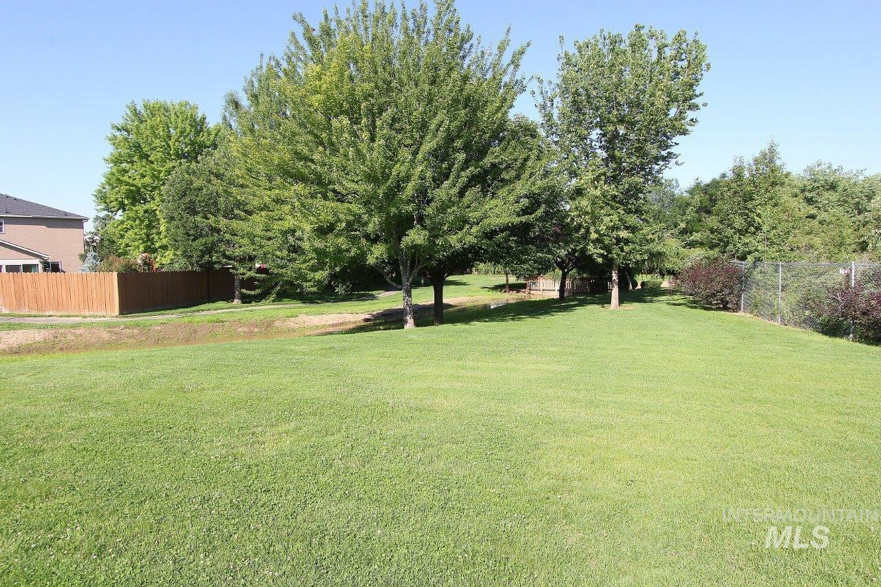 Expansive green lawn with mature trees and a wooden fence bordering the property