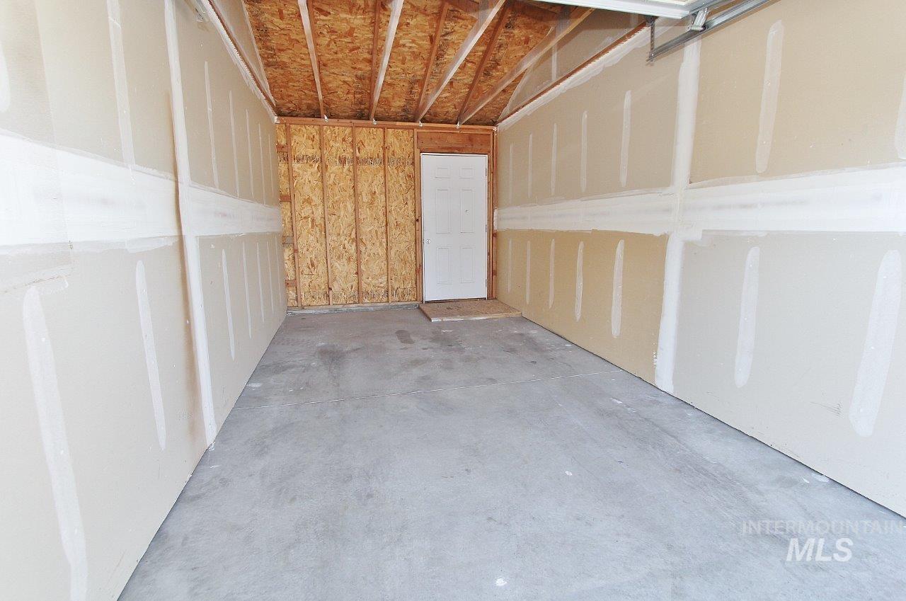 Spacious garage with concrete flooring, exposed wood ceiling beams, and a service door