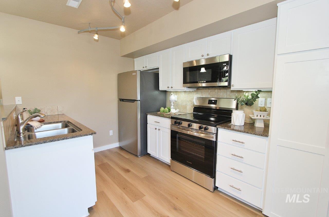 Kitchen featuring light wood-finish flooring, white cabinetry, stainless steel appliances, and granite countertops