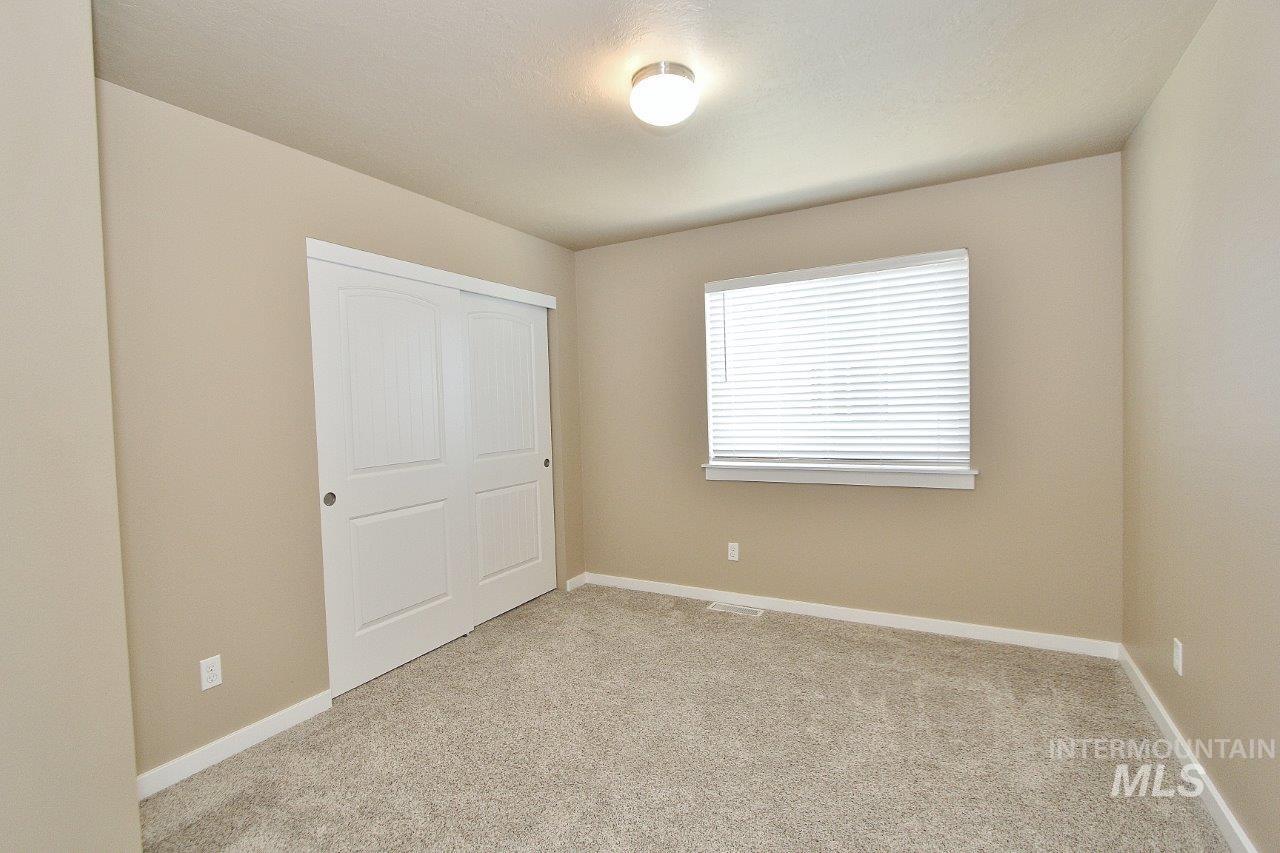 Neutral-toned room featuring light-colored carpet flooring, a window with horizontal blinds, and a white flush-mount ceiling light