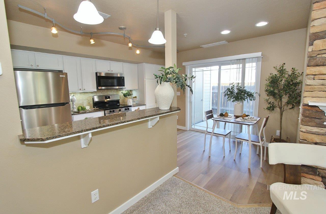Kitchen and dining area featuring a stone-look breakfast bar with a granite-style countertop, stainless steel appliances, light wood-finish flooring, and a sliding glass door to the exterior