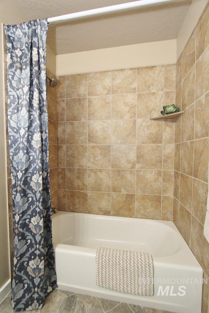 Bathtub and shower combination featuring neutral-toned tile surround, integrated shower shelf, and gray-toned floor tiling