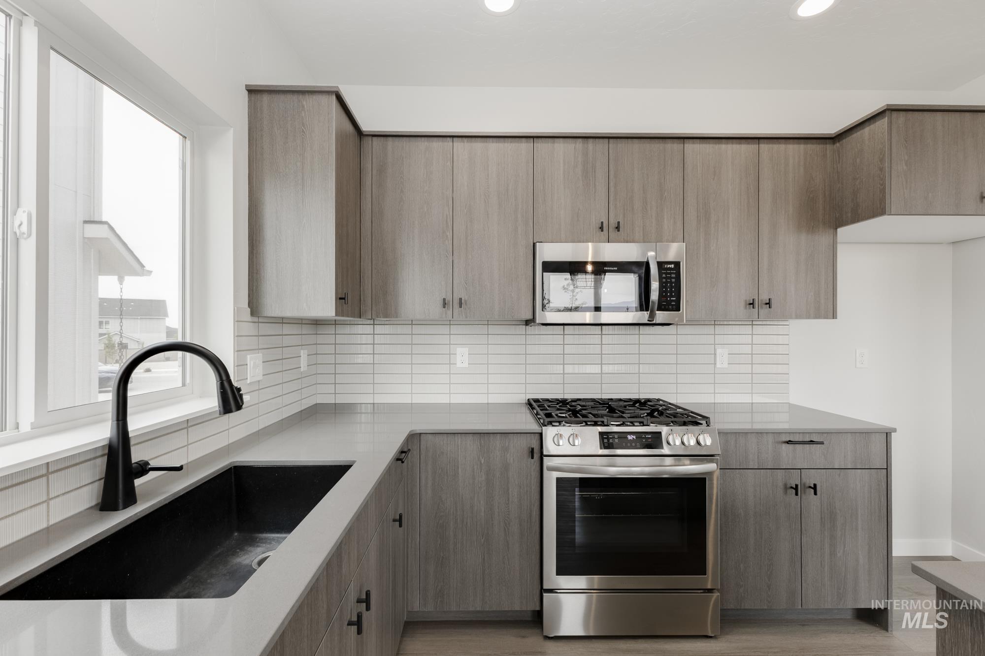 Kitchen with appliances with stainless steel finishes, tasteful backsplash, light wood-style flooring, light stone countertops, and recessed lighting