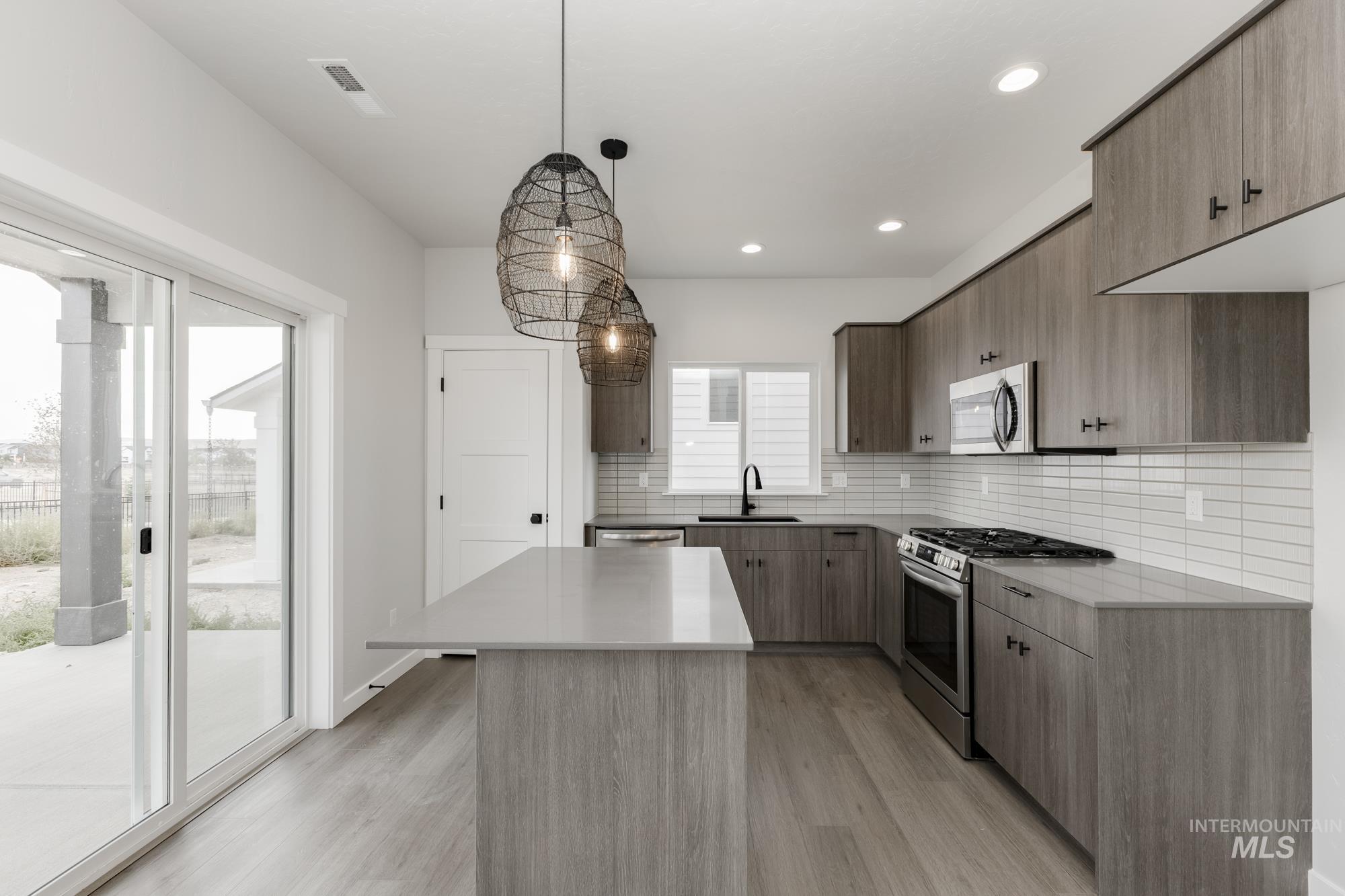Kitchen with appliances with stainless steel finishes, pendant lighting, backsplash, light wood finished floors, and recessed lighting