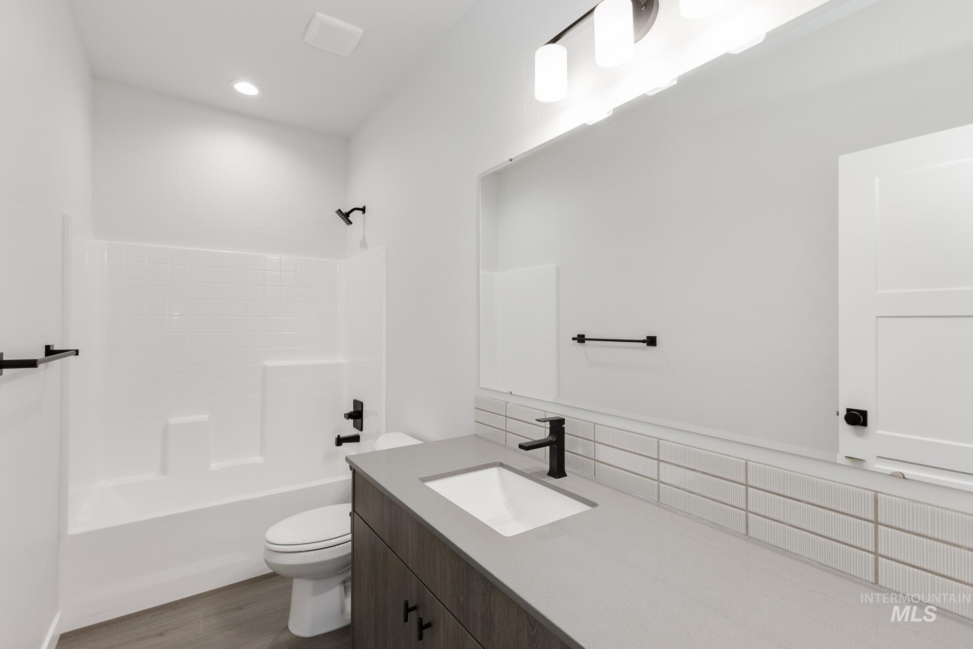 Bathroom featuring vanity, bathtub / shower combination, dark wood-type flooring, and recessed lighting