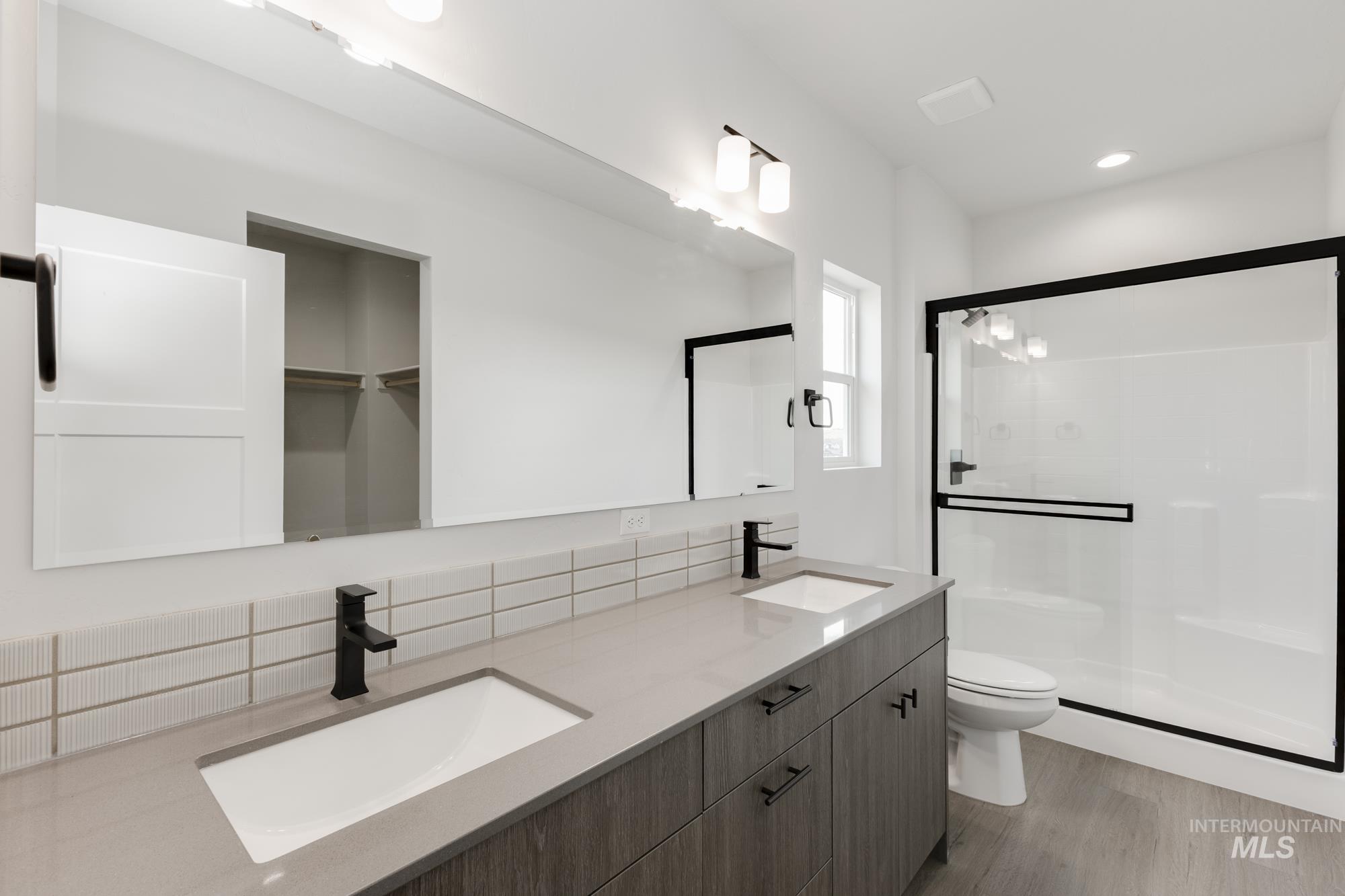 Full bath with a stall shower, double vanity, a walk in closet, light wood-style floors, and tasteful backsplash