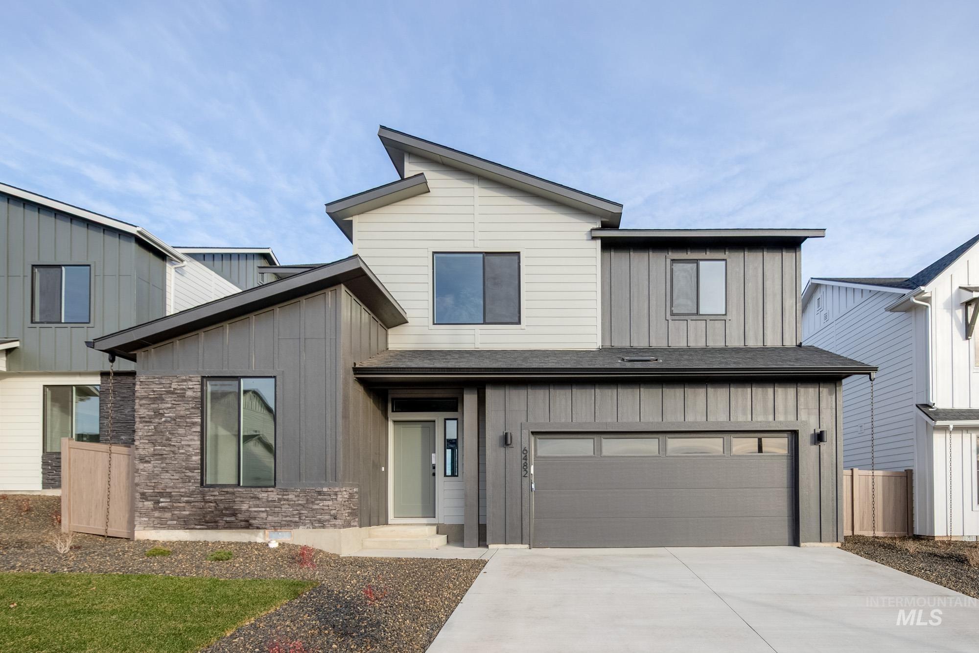 View of front of home with board and batten siding, an attached garage, concrete driveway, stone siding, and a shingled roof