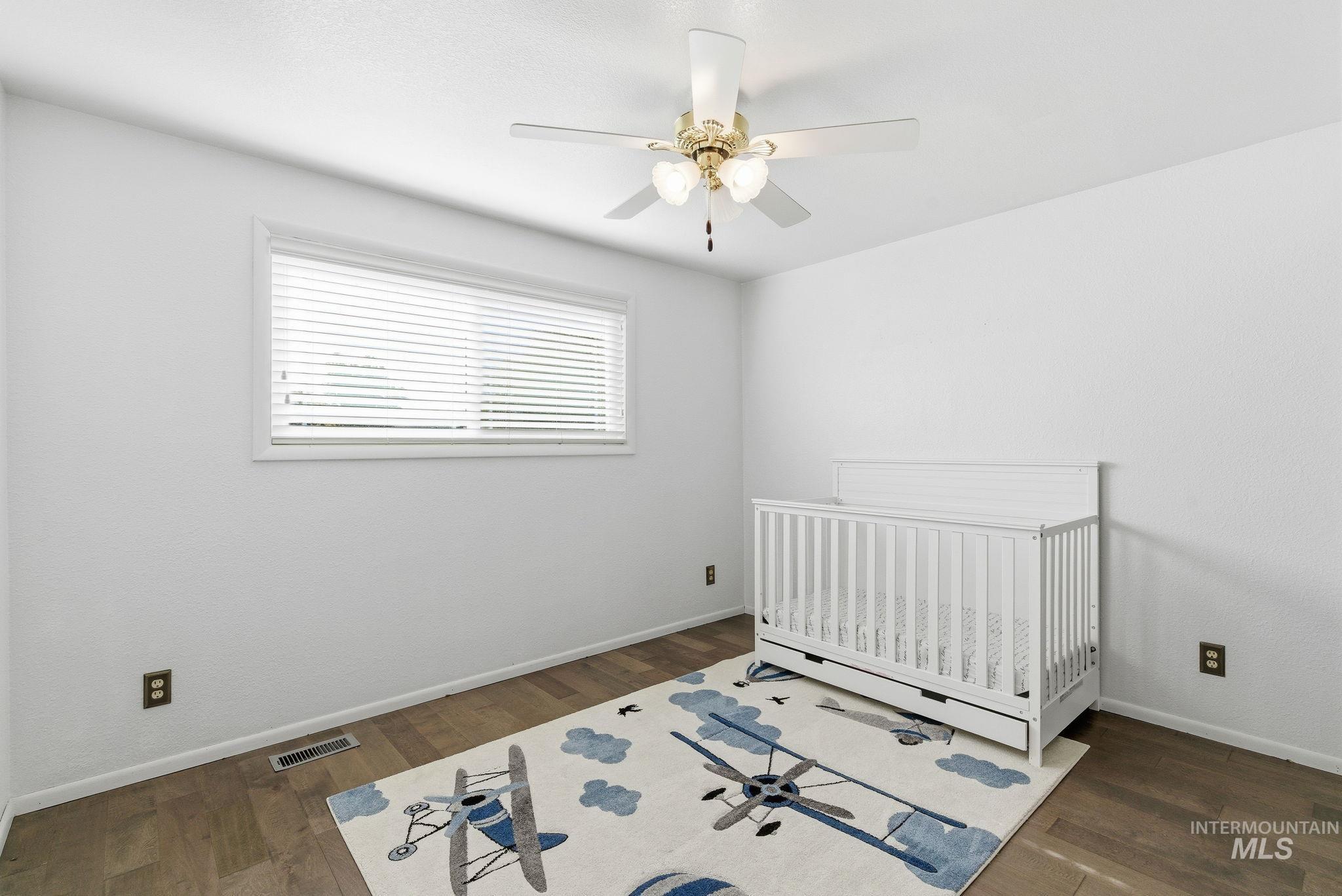 Bedroom with a nursery area, dark wood-style floors, and ceiling fan