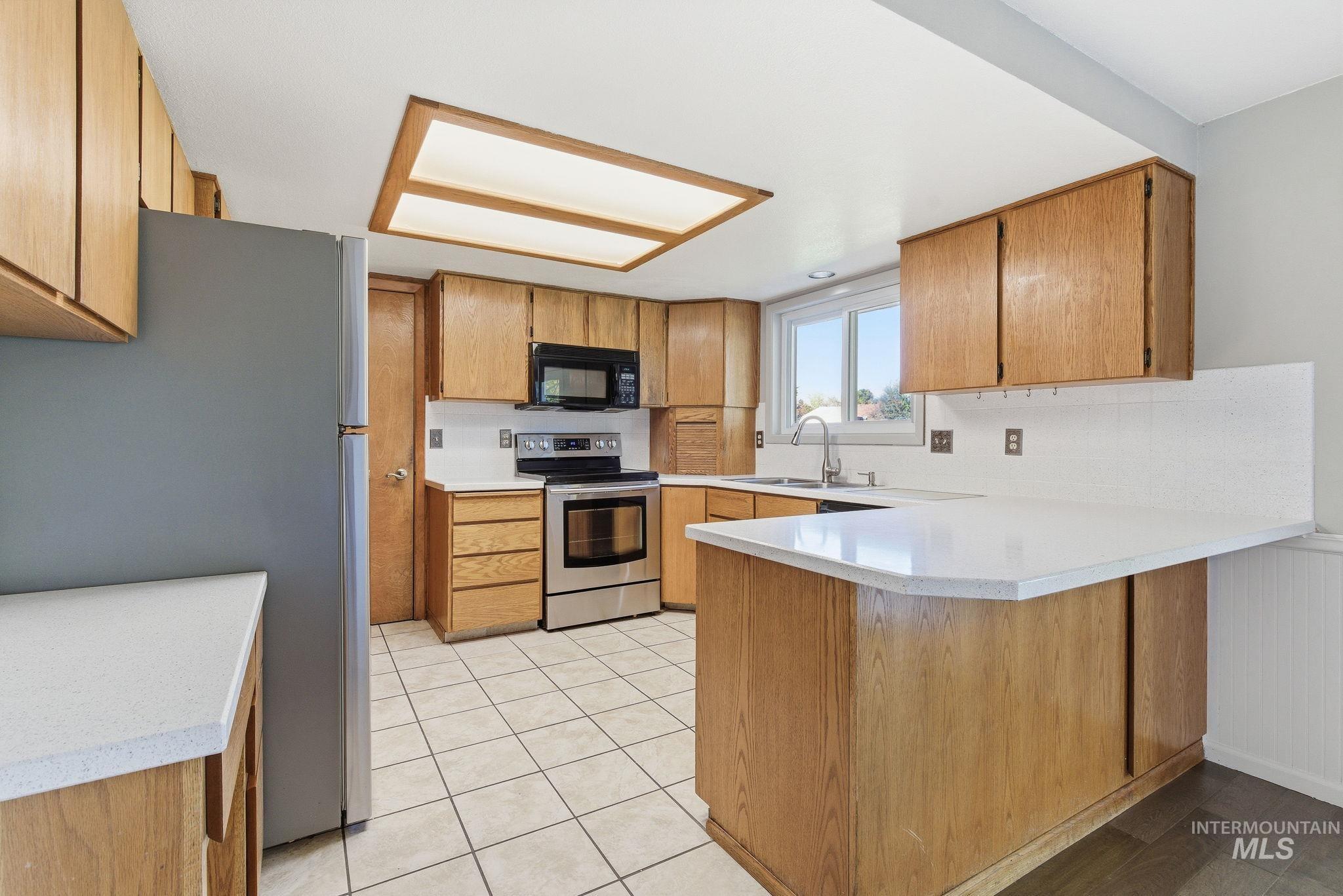 Kitchen with a peninsula, appliances with stainless steel finishes, brown cabinets, light tile patterned flooring, and a breakfast bar area