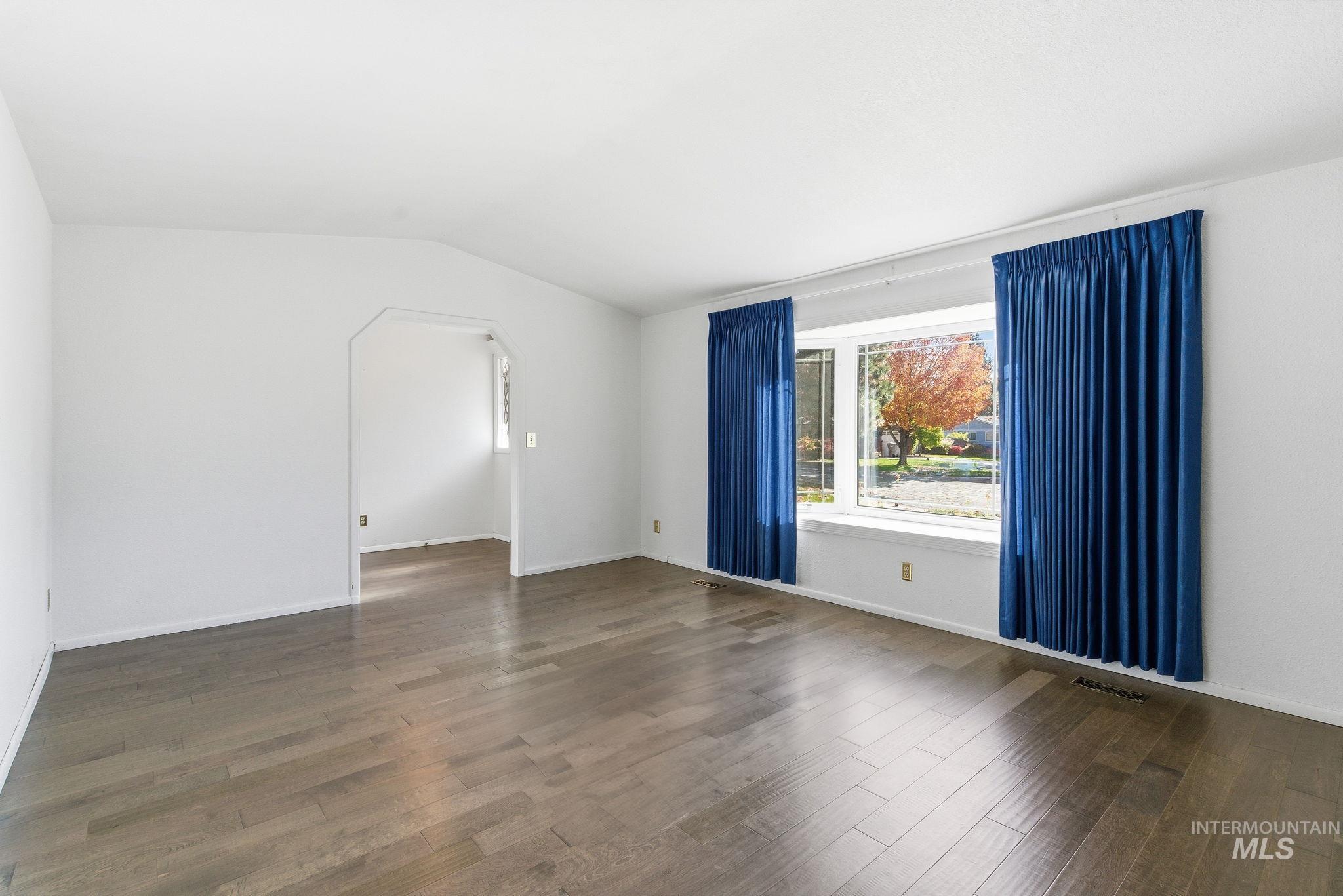 Empty room featuring arched walkways, dark wood-style floors, and lofted ceiling