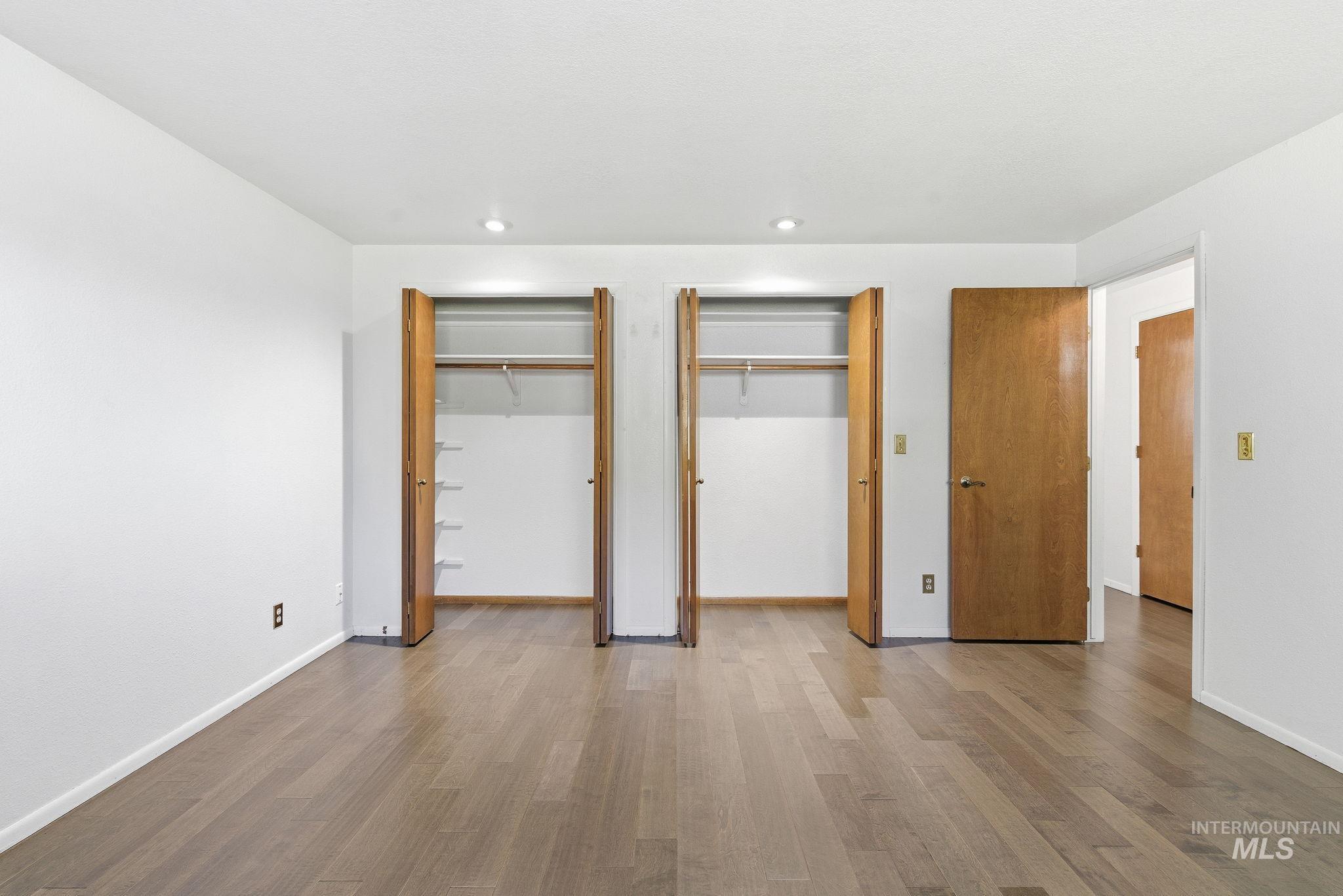 Unfurnished bedroom with two closets, wood finished floors, and recessed lighting