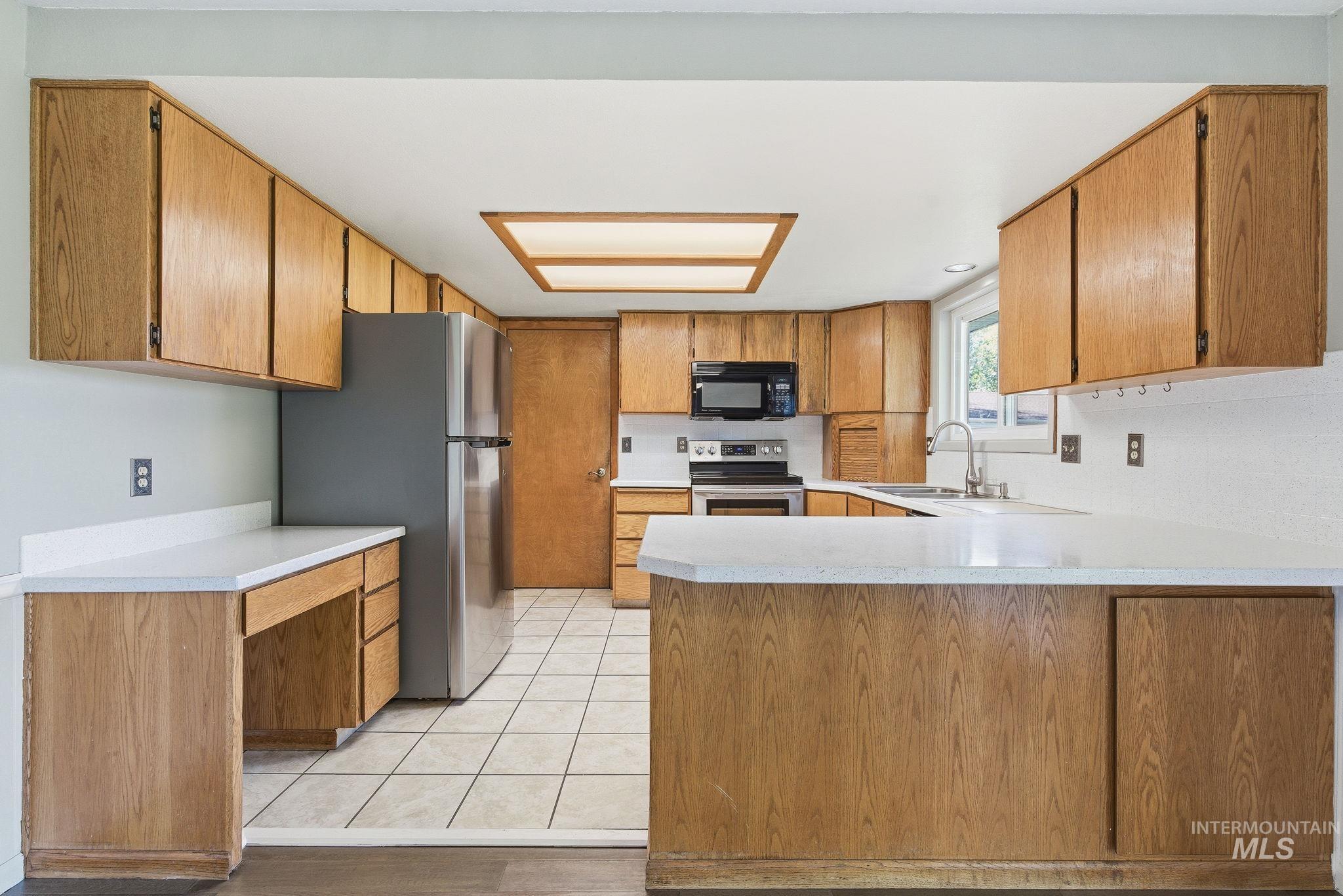 Kitchen with a peninsula, light countertops, appliances with stainless steel finishes, brown cabinets, and light tile patterned flooring