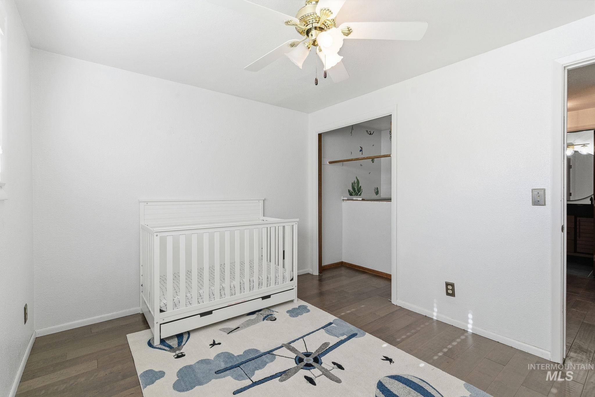 Bedroom with a crib, dark wood-style floors, and ceiling fan