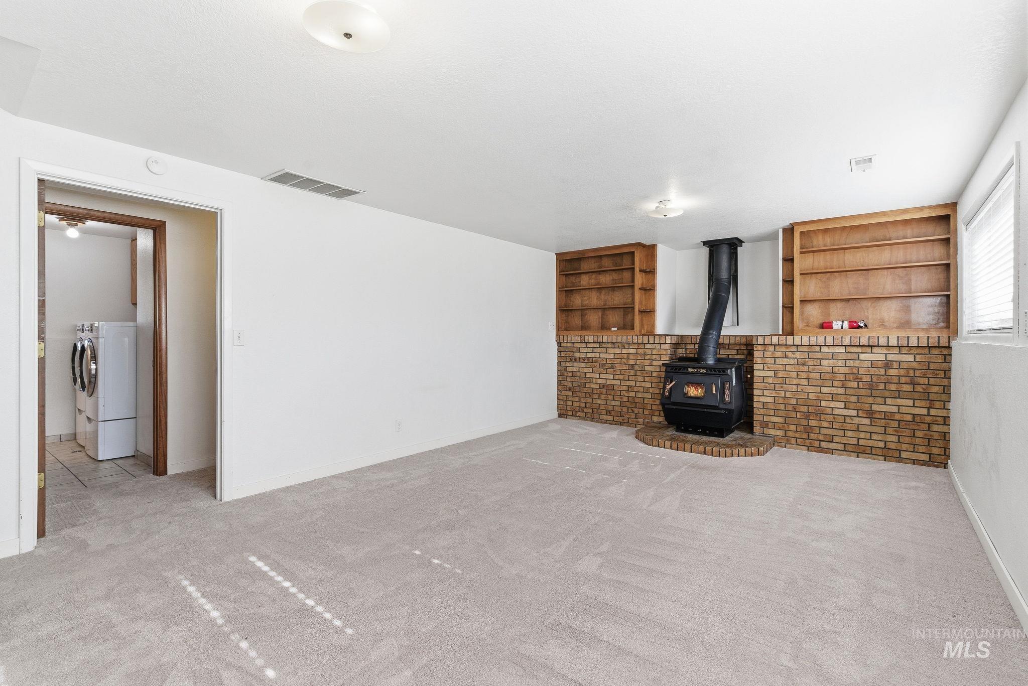 Unfurnished living room featuring a wood stove, carpet, built in features, and washer and clothes dryer
