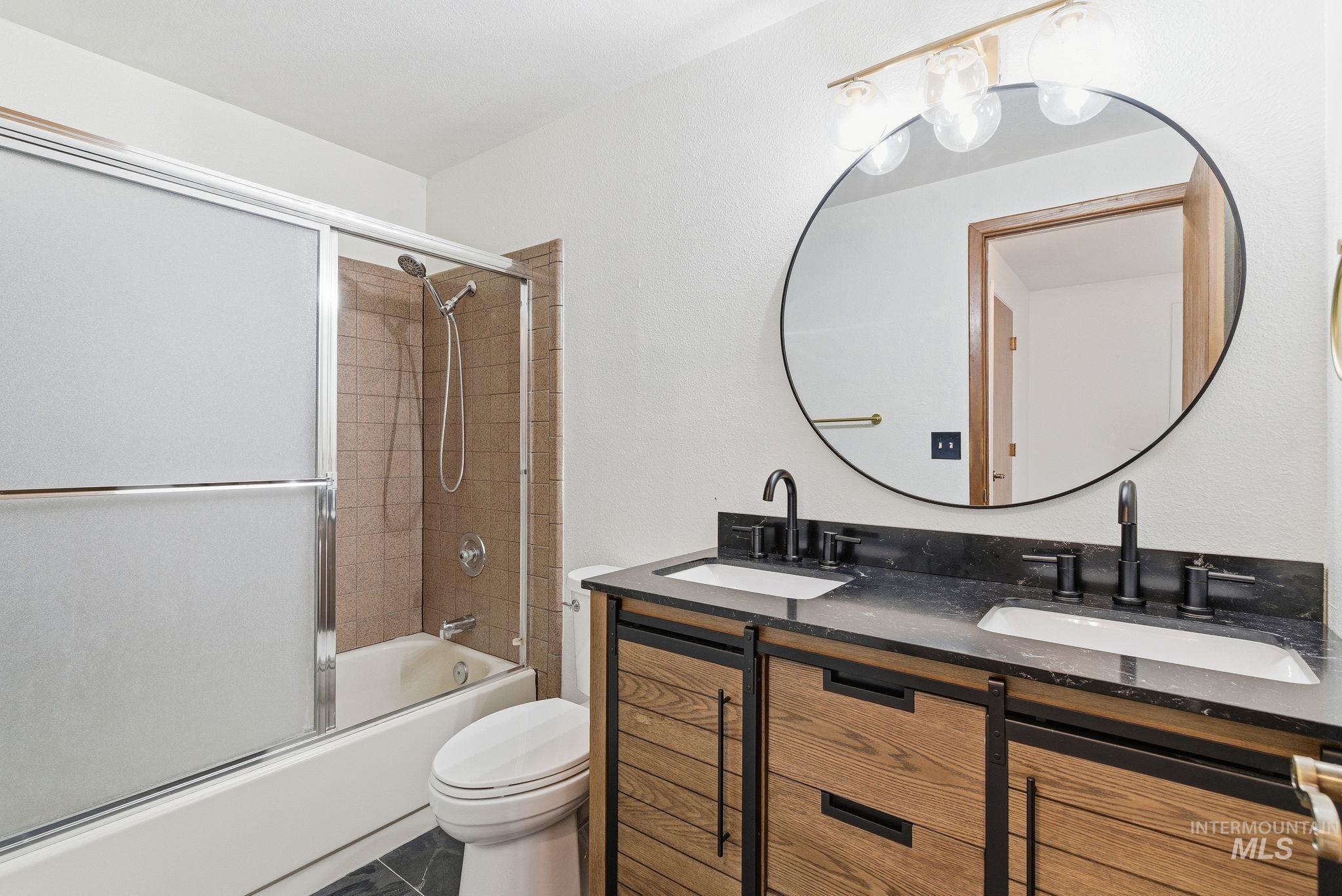 Bathroom with combined bath / shower with glass door, double vanity, and dark tile patterned floors