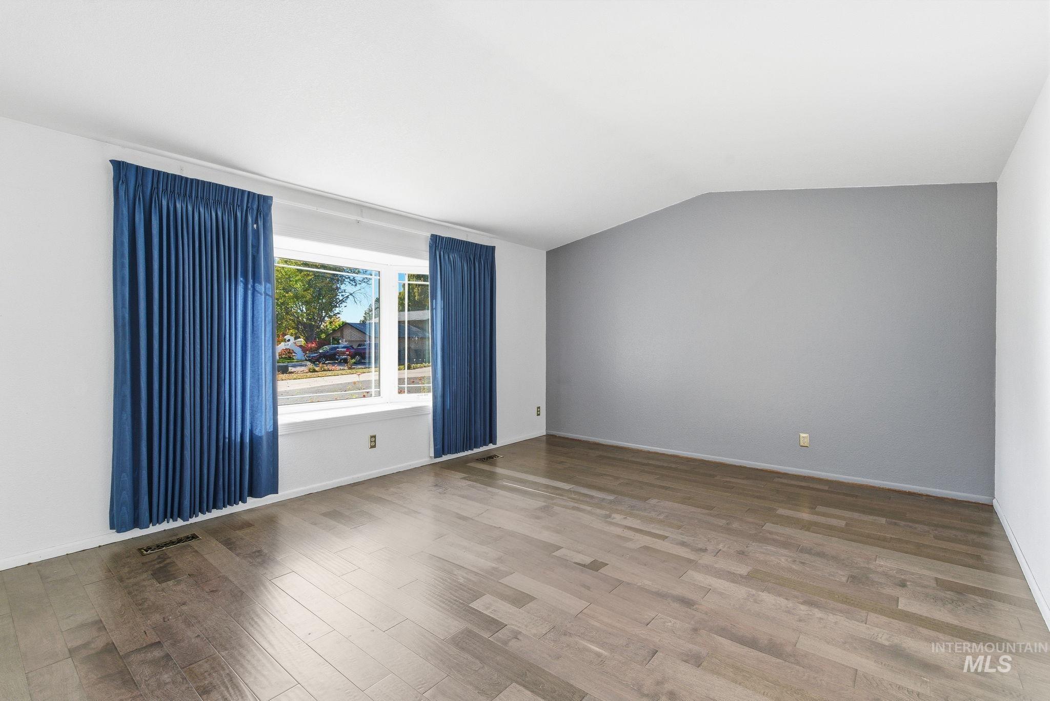 Spare room featuring wood finished floors and vaulted ceiling