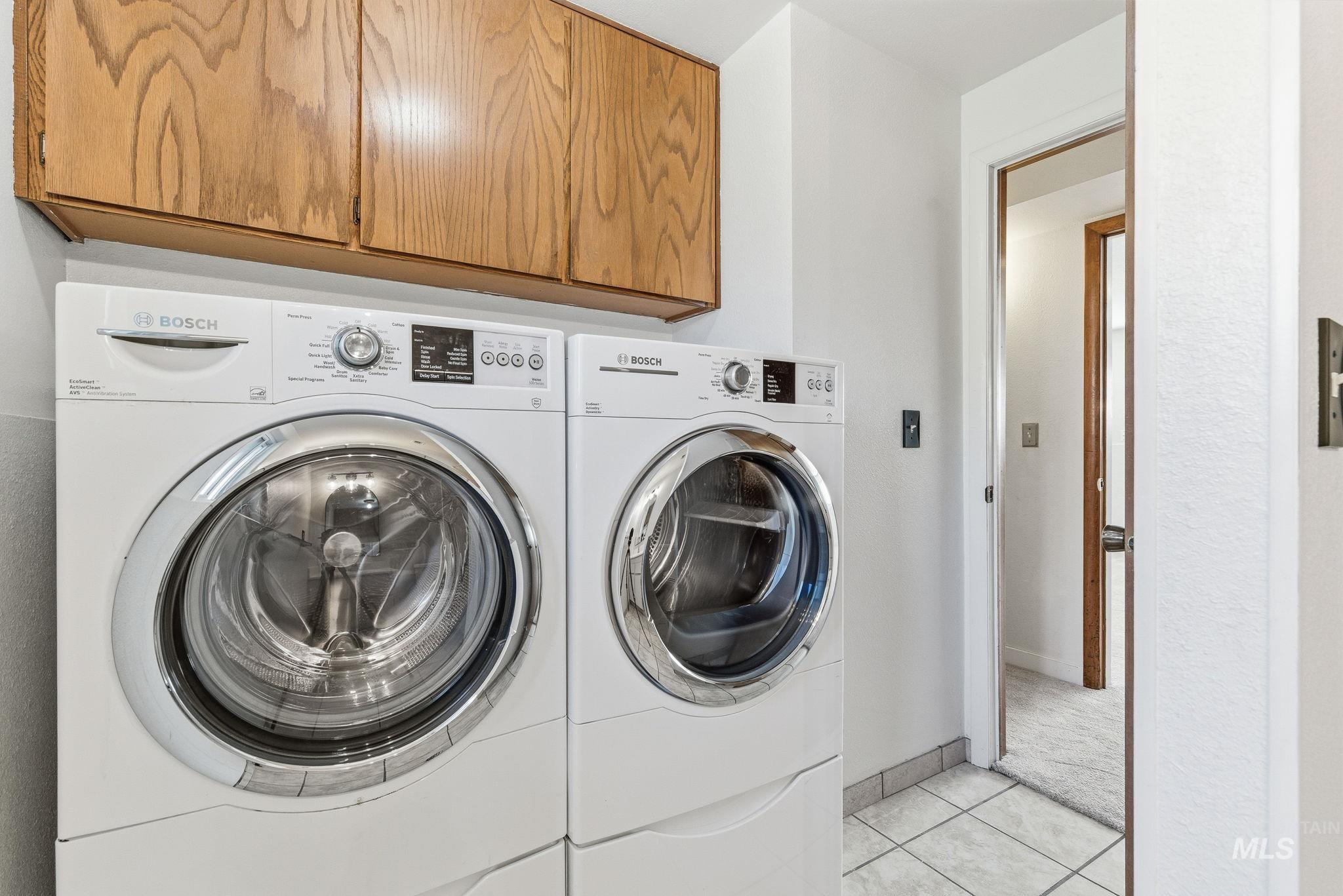 Washroom featuring light tile patterned floors, cabinet space, and washing machine and clothes dryer