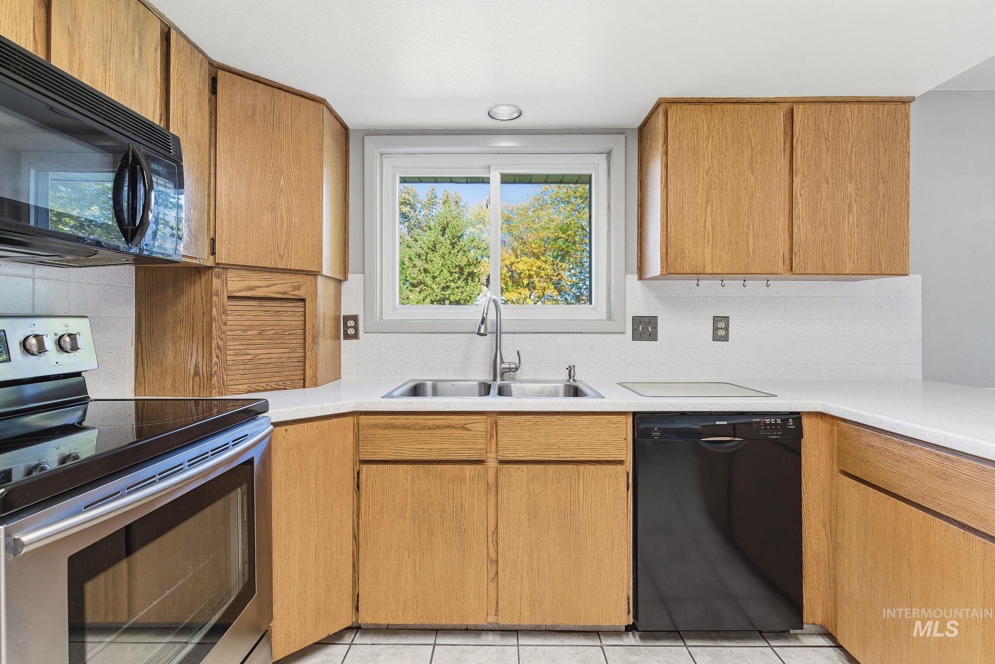 Kitchen featuring black appliances, tasteful backsplash, light countertops, and light tile patterned floors